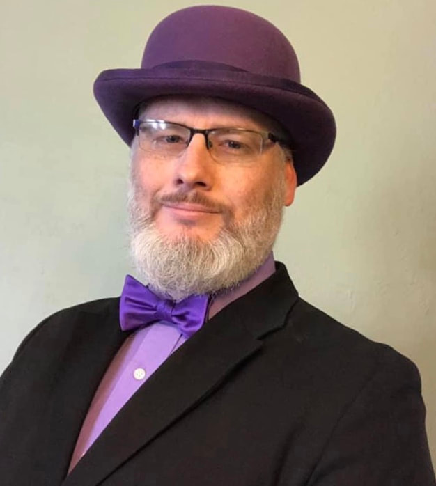 Justin, a white male with gray hair and beard, eyeglasses. He is wearing a purple Bowler hat with purple bow tie, purple dress shirt, and black suit. With a light green background.