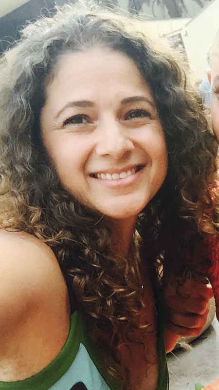 Image description: A slightly tan skinned Mexican / American woman in her 40’s with brown and thick curly hair. She is smiling and wearing a green, light blue and darker brown striped tank dress
