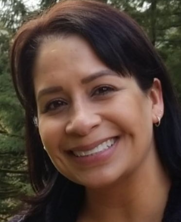 Hispanic female smiling at the camera, has shoulder length dark brown hair and dark brown eyes.