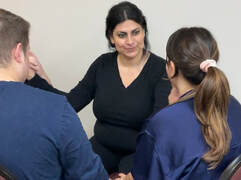 Lesley, a DeafBlind Latina woman, smiles while using Protactile language with two others