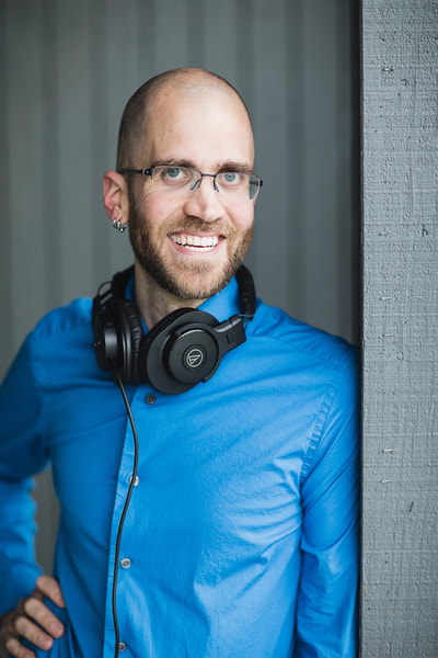 Gerard: Male, close cropped brown hair and beard, blue eyes. Bright blue dress shirt with AudioTechnica headphones around his neck.