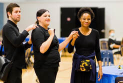 Sarah, a Caucasian woman in dark clothing, is smiling and standing with two other people using Protactile Language.