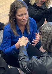 Rho, a brunette middle-aged white woman wearing a bright blue shirt, using Protactile language with another person.