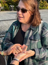 Kelly, a white woman with brown-reddish hair, a plaid shirt, and sunglasses, smiling slightly as she signs using Protactile language on someone’s palm.